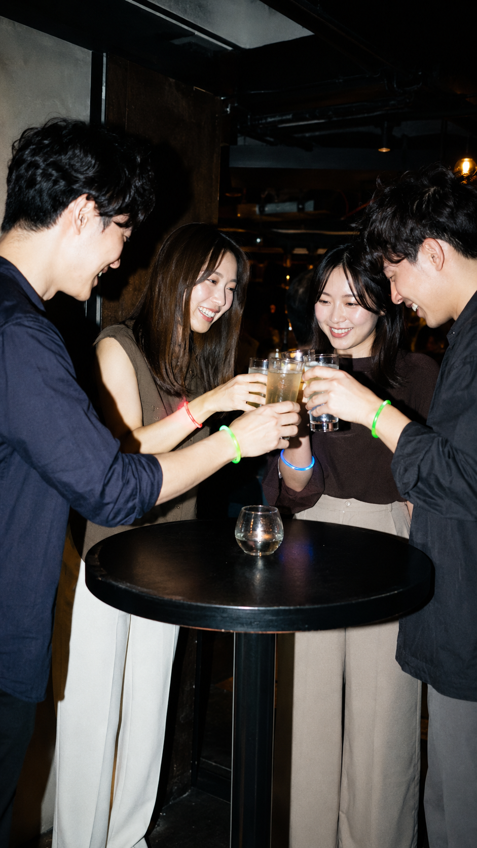 男女4人が立食テーブルを囲み自然な笑顔で乾杯する様子
